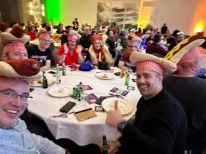 An image showing a group of people sat at the table, wearing hot-dog hats