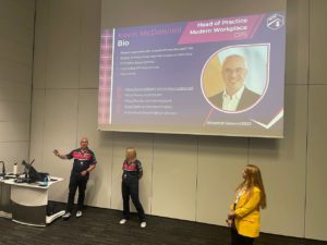 two women and a man presenting on stage in front of a big screen